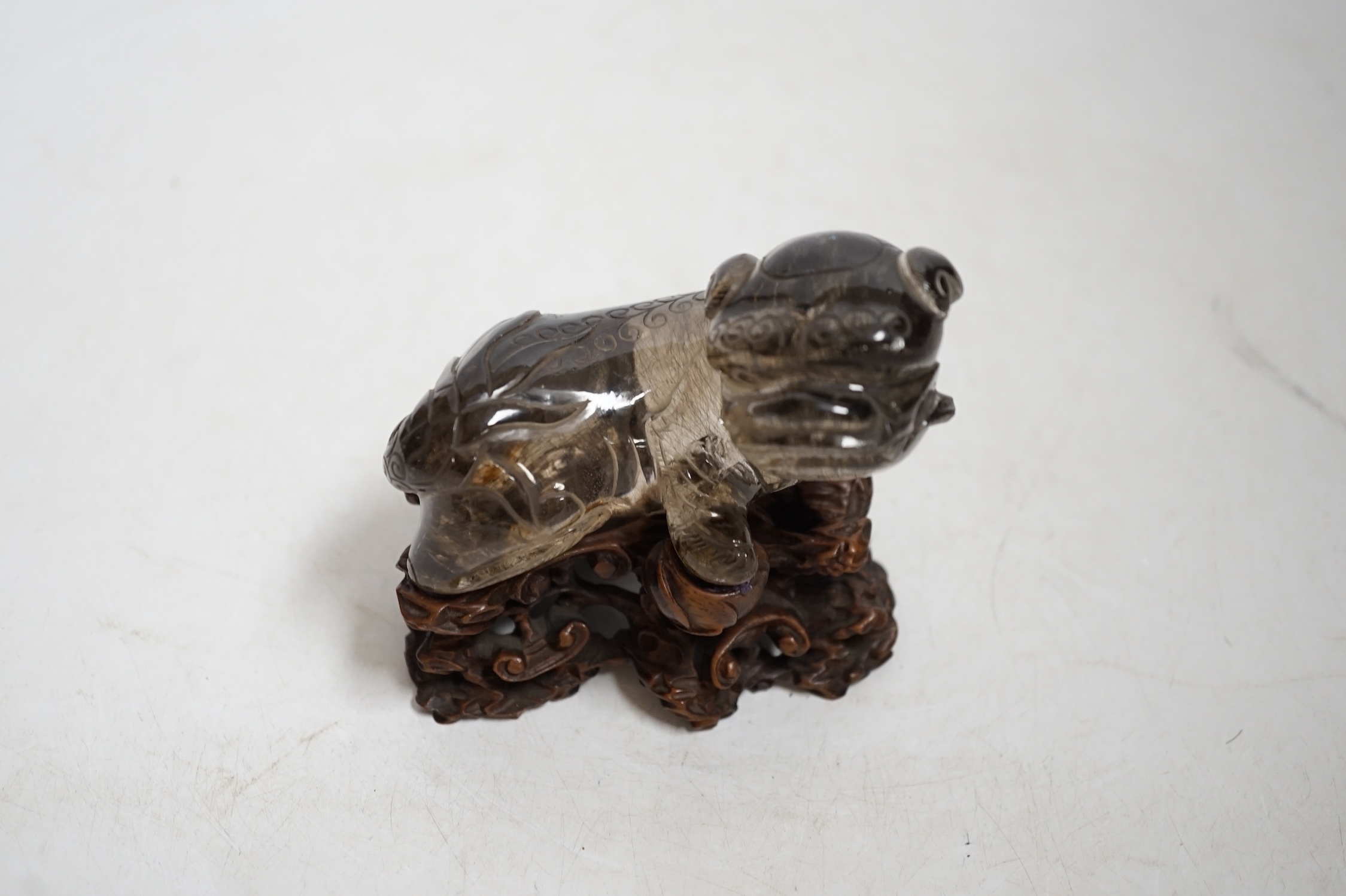 A Chinese carved smoky quartz lion dog on hardwood stand, 9.5cm wide. Condition - fair, impact damage to tail